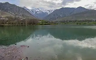 A lake with a mountain in the background, surrounded by green trees. Sky is overcast.