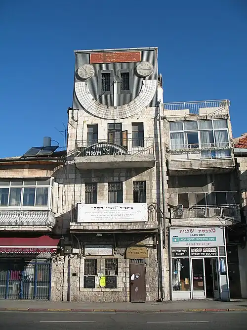 A narrow, four-story-high building with a large sundial on the fourth floor