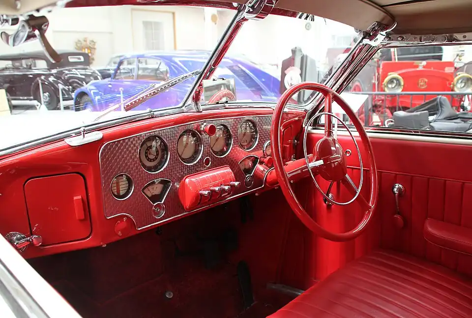 The interior of a 1937 Cord 810 with a red steering wheel equipped with a silver horn ring.