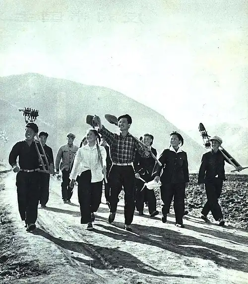 Smiling young people carrying tools down a road
