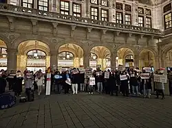 A crowd stands with German and Korean language signs in Vienna, Austria