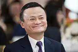 Jack Ma wearing a navy blue suit and matching patterned tie with a white shirt while smiling.