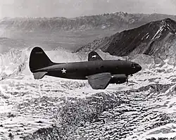 Black and white photograph of the right side of a plane flying over a mountainous region