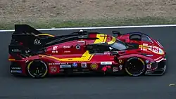Colour photo of a Ferrari 499P Hypercar in a red livery with yellow details.
