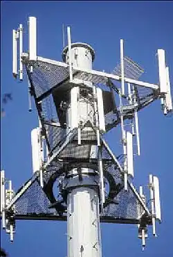 Sector antennas (white bars) on cell phone tower. Collinear arrays of dipoles stacked inside the tall white cases radiate a flat, fan-shaped beam.