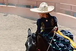 A Mexican Escaramuza charra wearing a sombrero in a chareada