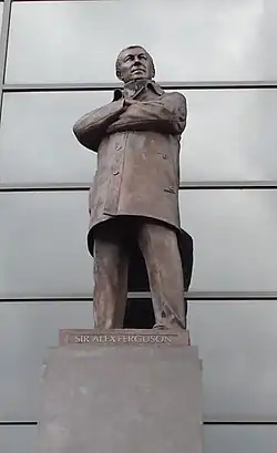 A bronze statue of a man wearing a coat with his arms folded.