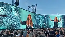 Adele appears on a blue-green background on a giant screen