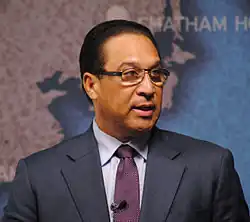 Photograph of a man, Alden McLaughlin, wearing a suit and a small microphone at a speaking event