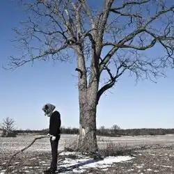 A man in an animal mask holding a stick in front of a tree