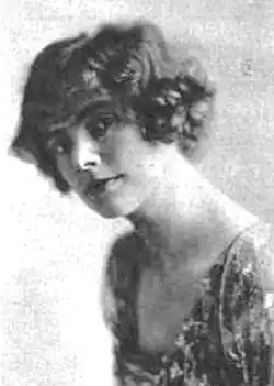 A young white woman with bobbed wavy hair, wearing a dress with a square neckline