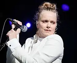 close-up of Ane Brun wearing a white outfit, holding a microphone onstage, looking left of camera