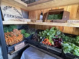 All wooden boxes stand with two-levels. They have wooden signs in cursive letters with details of what is being on display, with prices. The vegetables are a mixture of carrots, beets, cilantro, lettuce, and dill.