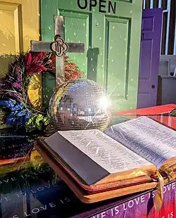 A church altar decorated with a disco ball and colors celebrating LGBTQ pride.