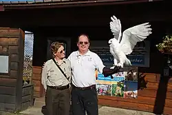 A park ranger and a man standing in front of a visitor's centre. The man is holding a snowy owl.