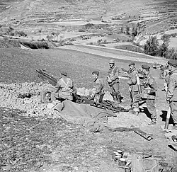 Gun in pit surrounded by crew on a hillside