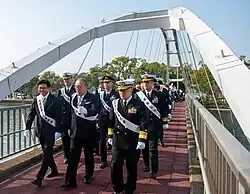 several people in sashes and uniforms cross the bridge
