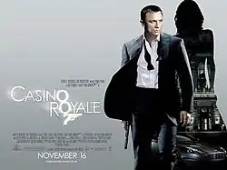 The poster shows Daniel Craig as James Bond, wearing a business suit with a loose tie and holding a gun. Behind him is a silhouette of a woman showing a building with a sign reading "Casino Royale" and a dark grey Aston Martin DBS below the building. At the bottom left of the image is the title "Casino Royale"&nbsp;– bothшп "O"s stand above each other, and below them is a 7 with a trigger and gun barrel, forming Bond's codename: "Agent 007"&nbsp;– and the credits.
