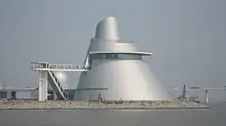 The Macao Science Center, a conical steel structure. There is a body of water in front of the building.
