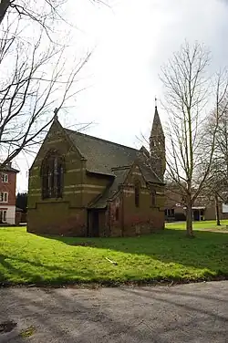 A photograph of a brown building with a sloped roof and a tower protruding from the right portion of the roof all surrounded by green grass