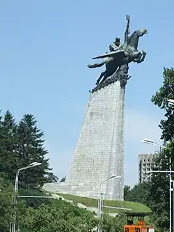 Statue of two people riding a horse with wings, one of whom is holding a book