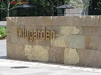 The word "Citygarden" in gold metal letters is fixed to a low wall made of golden-yellow rock bricks.