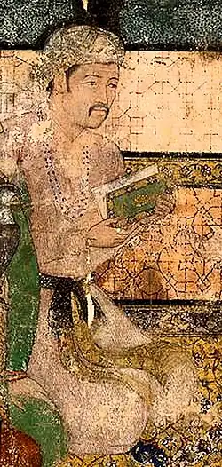 A seated man with moustache, holding a book.