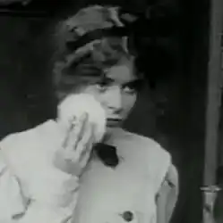 Black and white film still showing a woman in 1912 period dress