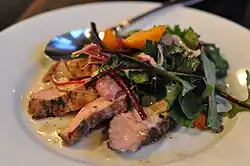 Dressed and slightly wilted greens served on top of sliced pork garnished with peaches