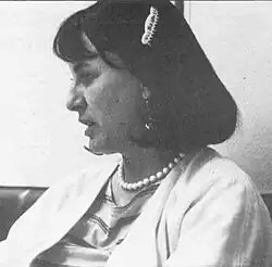 Profile of a woman in a business suit wearing a pearl necklace and dangling earrings