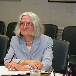 Dr. Susan Koch sitting at a table in a meeting room with a pen in her hand over a folder of papers.