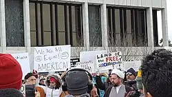 Crowd of people in Dearborn Michigan. Signs are visible, including one reading "We are all equal! America!" and "Land of the free? #NoBanNoWall"