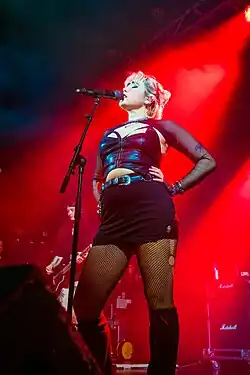 Alexia Roditis is on stage, wearing black in red lighting, singing into a microphone on a stand.