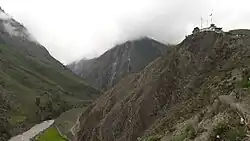 Photo of a mountain range with a river and a small settlement at the top of one mountain