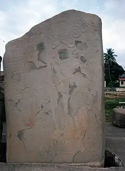 An upright stone slab with faint relief sculpture, badly flaked in places.
