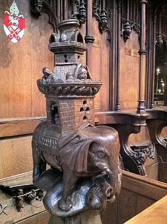A carved wooden elephant with a very tall castle on its back, and small figures peering out over the battlements