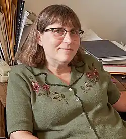 Photo of a woman with glasses and long hair wearing a green blouse