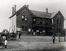 A black and white photo of a grand brick building as viewed from a short distance away with people and a horse and cart in front. A sign on the building says "GREAT NORTHERN RAILWAY".