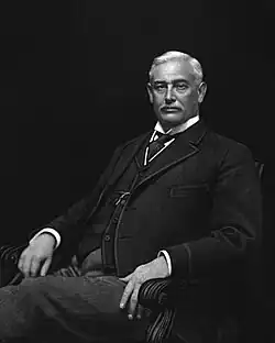 A black-and-white lithographic portrait of an older, mustached man, seated, wearing a suit, with a necktie