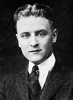 Photograph of F. Scott Fitzgerald as a student at Princeton. The photo features only his head and shoulders. He is wearing a dark tie and a pin-striped suit. His hair is parted in the middle and neatly coiffed.