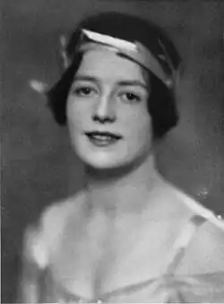 A young white woman with short dark hair, wearing a stylized laurel wreath and a low-cut satiny gown