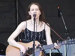 Welch singing and playing guitar on stage, wearing a black dress.