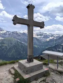 Big Summit Cross made of Stone on a Mountain Peak with some alpine peaks in the background
