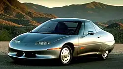 Picture of an unusually shaped concept car, taken in a mountainous environment with the sun setting.
