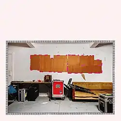 A beige-walled room in the Hotel2Tango studio, with a long table cluttered with equipment, a vintage mustard sofa, and cardboard taped to the wall with pink tape.
