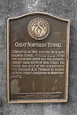 A plaque that reads, "Great Northern Tunnel - Completed in 1905, this one mile long railroad tunnel provided access to the new passenger depot and the expanded freight yards south of King Street. The tunnel was built at the suggestion of city engineer R. H. Thomson to relieve growing street congestion in downtown Seattle."