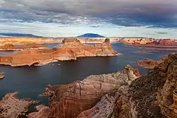 Aerial view of tall red rock mesas rising above the reservoir with a cloudy sky