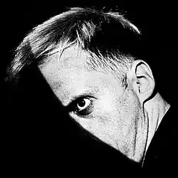 A portrait of the artist in black and white with his face half obscured