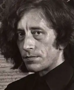 Three-quarter profile, sepia, dramatic publicity shot of an unsmiling, clean-shaven man with big hair and dark eyes. He looks directly at camera with a smouldering expression.