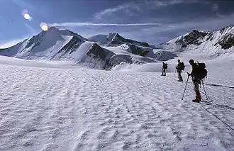Three mountaineers on a snow-covered icefield with mountain peaks in the distance